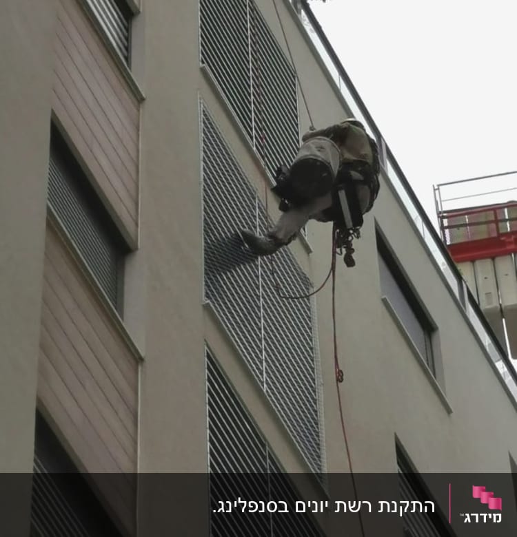 אדם תלוי על חבל ליד תריסים בבניין גבוה